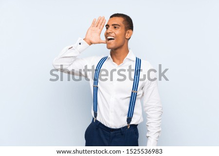 Young handsome brunette man with suspenders over isolated background shouting with mouth wide open
