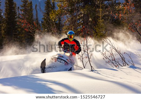 the guy is flying and jumping on a snowmobile on a background of winter forest  leaving a trail of splashes of white snow. bright snowmobile and suit without brands. extra high quality Royalty-Free Stock Photo #1525546727