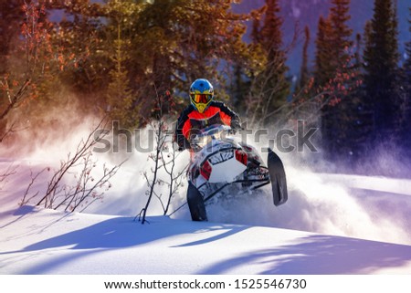 the guy is flying and jumping on a snowmobile on a background of winter forest  leaving a trail of splashes of white snow. bright snowmobile and suit without brands. extra high quality Royalty-Free Stock Photo #1525546730