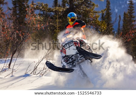 the guy is flying and jumping on a snowmobile on a background of winter forest  leaving a trail of splashes of white snow. bright snowmobile and suit without brands. extra high quality Royalty-Free Stock Photo #1525546733