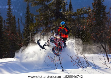 the guy is flying and jumping on a snowmobile on a background of winter forest  leaving a trail of splashes of white snow. bright snowmobile and suit without brands. extra high quality Royalty-Free Stock Photo #1525546742