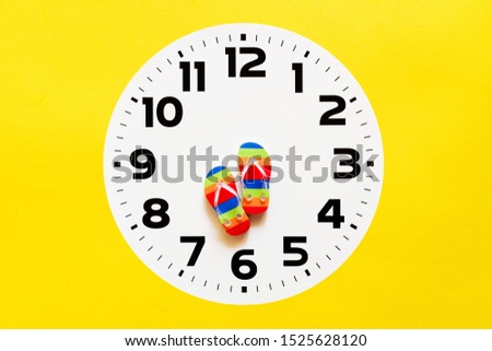Bright flip flops in the form of arrows on the white dial of hours. Time to have a rest, time of vacation. Conceptual image of rest, holiday, summer vacation. 
