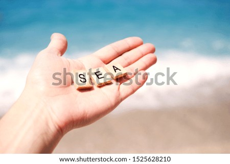 The word SEA is laid out on wooden cubes on a female hand on a background of the sea. Sea summer vacation