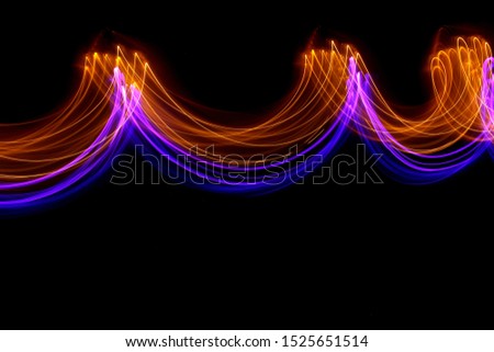Long exposure photograph of neon purple and gold colour in an abstract swirl, parallel lines pattern against a black background. Light painting photography.
