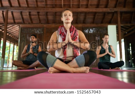 Beautiful woman teaching meditation to two multi-ethnic men on yoga mats in traditional temple in Bali Indonesia Royalty-Free Stock Photo #1525657043