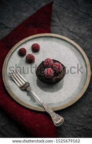 Chocolate fondant with frozen raspberries on a plate. Grey and red flax napkins, fork. A stylized photo with film effect filter.