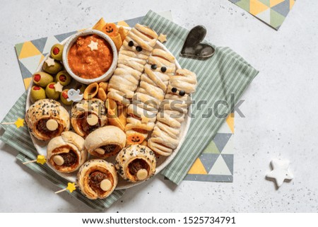Scary sausage mummies in dough with funny eyes on table. Halloween food. Top view. Flat lay