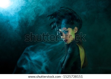 Portrait of Model in a headdress 
with feathers. Сoncept for rock musicians or music festival or Halloween party. Dark background, studio