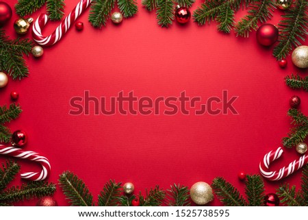 Christmas and New Year oval frame on red background. Festive decor of fir branches, Christmas balls and candy cane