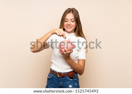 Young blonde woman over isolated background holding a big piggybank