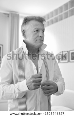 Smiling businessman buttoning shirt while looking away in bedroom at home