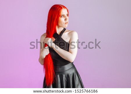 Girl with red long hair and leather skirt posing on pink background