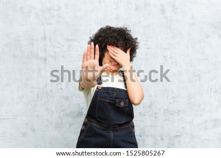 young pretty afro woman covering face with hand and putting other hand up front to stop camera, refusing photos or pictures