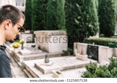 Stock photo of a a boy dressed in black and wearing sunglasses looking at a tomb in the cemetery of Bologna, Italy