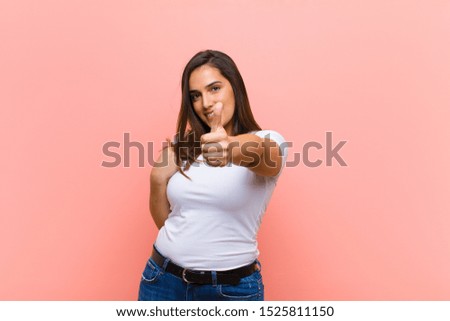 young pretty hispanic woman feeling proud, carefree, confident and happy, smiling positively with thumbs up against pink wall