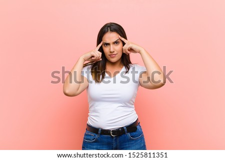 young pretty hispanic woman with a serious and concentrated look, brainstorming and thinking about a challenging problem against pink wall