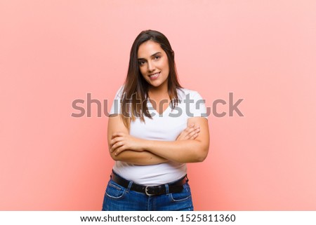 young pretty hispanic woman looking like a happy, proud and satisfied achiever smiling with arms crossed against pink wall