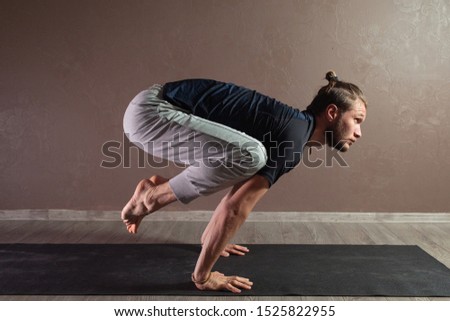 Young sporty man practicing yoga, meditating in Half Lotus pose, working out, wearing sportswear, indoor full length, brown yoga studio