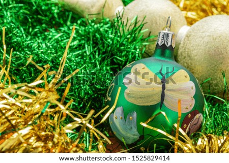 Background in the form of Christmas tree decorations - a large green painted ball, light beads, golden and green rain, side view, close-up
