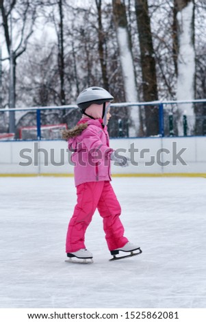 Beautiful girl having fun in winter park, balancing while skating at ice rink. Enjoying nature, winter time. Baby takes her first steps in figure skating