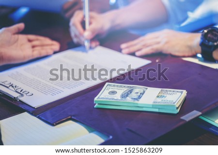 Businessman puts signature on contract at business meeting and passing money after negotiations with business partners. Selected focus to money