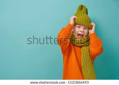 Winter portrait of happy child wearing knitted hat, snood and sweater. Girl having fun, playing and laughing on teal background. Fashion concept.