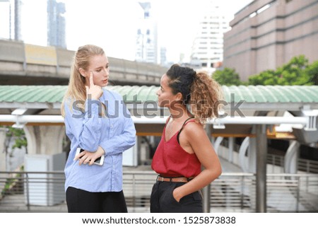 half shot of two caucasian businesswomen talking during lunch break while walking on walk way with city and skytrain background
