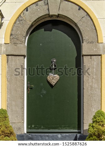 A vertical shot of an arch and a green door with a heart-shaped hanging ornament during daytime