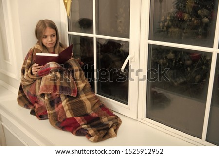 Happy Holidays. Little child read book on Christmas eve. Little girl enjoy reading Christmas story. Little reader wrapped in plaid sit on window sill. Childrens picture book. Magic xmas spirit.