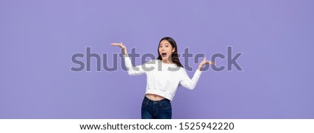 Beautiful excited young Asian woman doing presenting gesture with both hands open isolated on purple banner background
