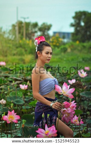 beautiful woman with Thai dress is holding pink lotus in the lotus field