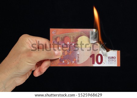 Hand holding a euro banknote burning conceptual picture on black background