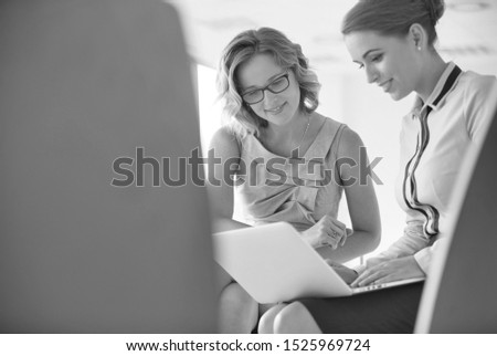 Black and white photo of Young businesswoman using laptop while sitting amidst colleagues at new office