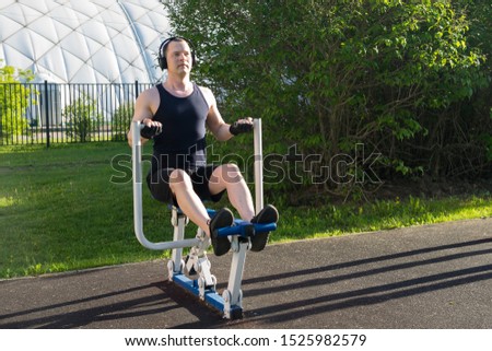 a man goes in for sports on the site, does an exercise on the simulator while listening to music