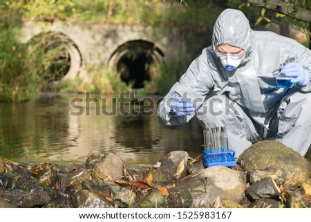 a man in a protective suit does an express test-tube test on the river bank