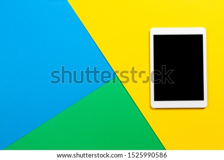 Digital tablet computer on light blue, green and yellow background. Top view