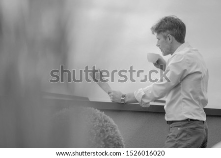 Black and white photo of businessman reading newspaper while drinking coffee in rooftop