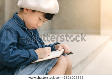 Closeup portrait of an artistic little asian schoolboy in stylish outfit and beret sitting on a stairs concentrate on his drawing or writing his diary. Child development, Cognitive skill, Neuroscience