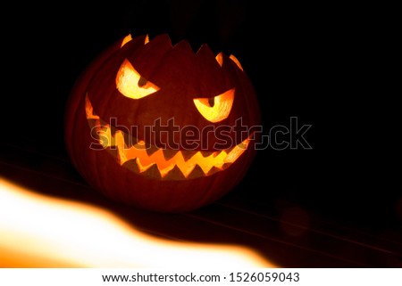 Spooky carved halloween pumpkin in hot burning hell fire flames with mad face, glowing eyes, mouth and teeth and evil smile.