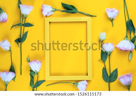 Empty yellow frame and flowers eustoma as layer on yellow paper background with copy space. Holiday concept