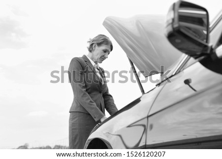 Black and white photo of Mature businesswoman looking at breakdown car on road