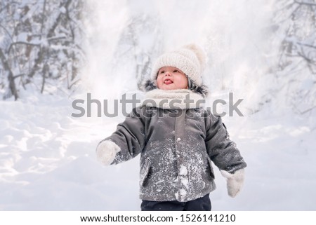 Little boy stands in winter forest and catches snowflakes with h