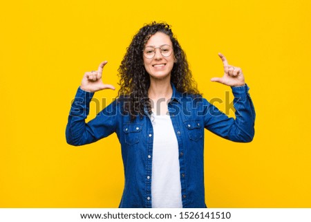 young pretty woman framing or outlining own smile with both hands, looking positive and happy, wellness concept against orange wall