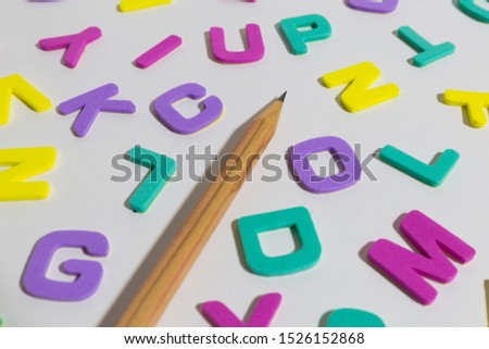 Wooden pencil and scattered alphabet letters on plastic sticker on white background