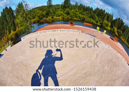 the sandy surface of the beach play area is formed by bright daylight, which falls under the shadow of the silhouette of the photographer who photographed himself on the fisheye lens.