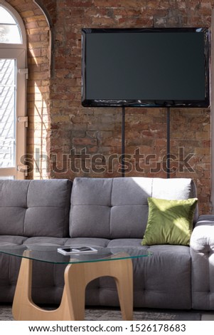 Mock up blank empty television screen on the brown brick wall background with sofa and sunlight. Copyspace, negative space for your advertising. Business, office style.