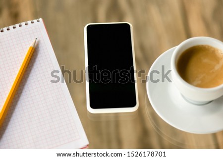 Mock up empty black smartphone screen on wooden table background with pencils, notes and cup of coffee. Copyspace, negative space for your advertising, office and business style.