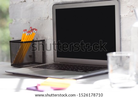 Mock up empty black laptop screen on white brick wall background with pencils, notes and glass of water. Copyspace, negative space for your advertising, office and business style.
