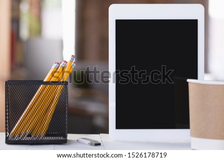 Mock up empty black tablet screen on blured background with pencils and cup of coffee. Copyspace, negative space for your advertising, office style.