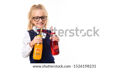 A little girl with blond hair stuffed in a horse tail, large blue eyes and a cute face in square black glasses keeps orange and watermelon juice in a glass bottle.